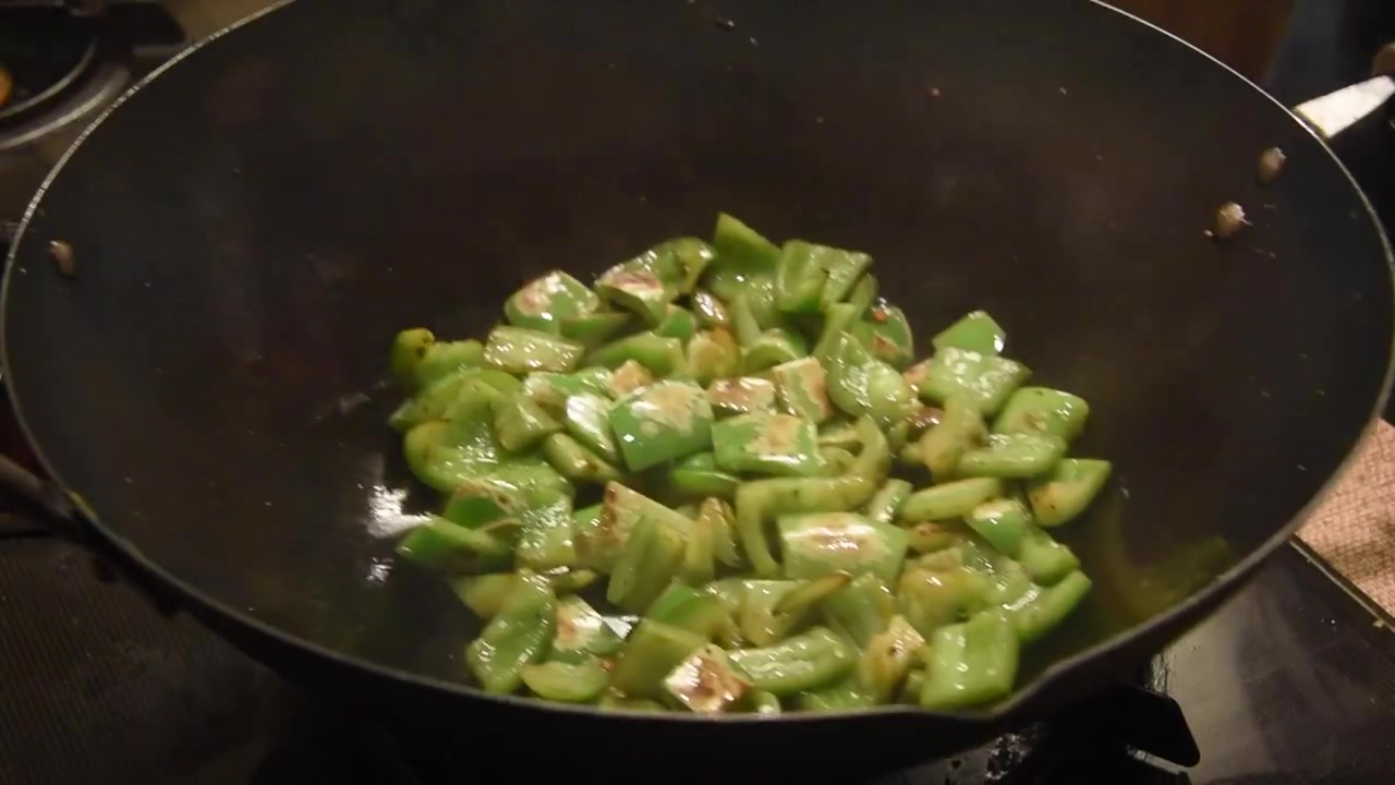 Professional chef stir-frying chopped green bell peppers in a traditional wok over a high-heat gas flame for a delicious asian dish