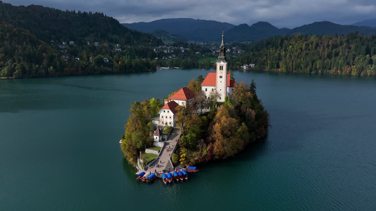 Panoramiczne ujęcie Zamku Bled wznoszącego się nad Jeziorem Bled ze spokojną wodą i alpejskimi górami w malowniczym krajobrazie Słowenii.