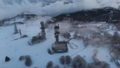 radio station with transmitter masts on snowy mountain in winter fog