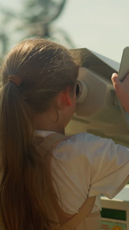 focused girl explores area popular for tourists through enormous binoculars. inquisitive child immersed in discovering spectacular mountainous terrain