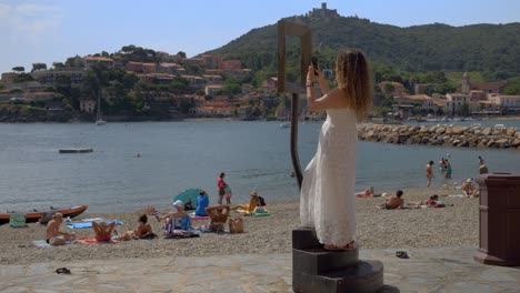 Mujer-Caminando-Hacia-El-Marco-De-La-Foto-Para-Tomar-Una-Foto-De-La-Playa-En-Collioure,-Francia