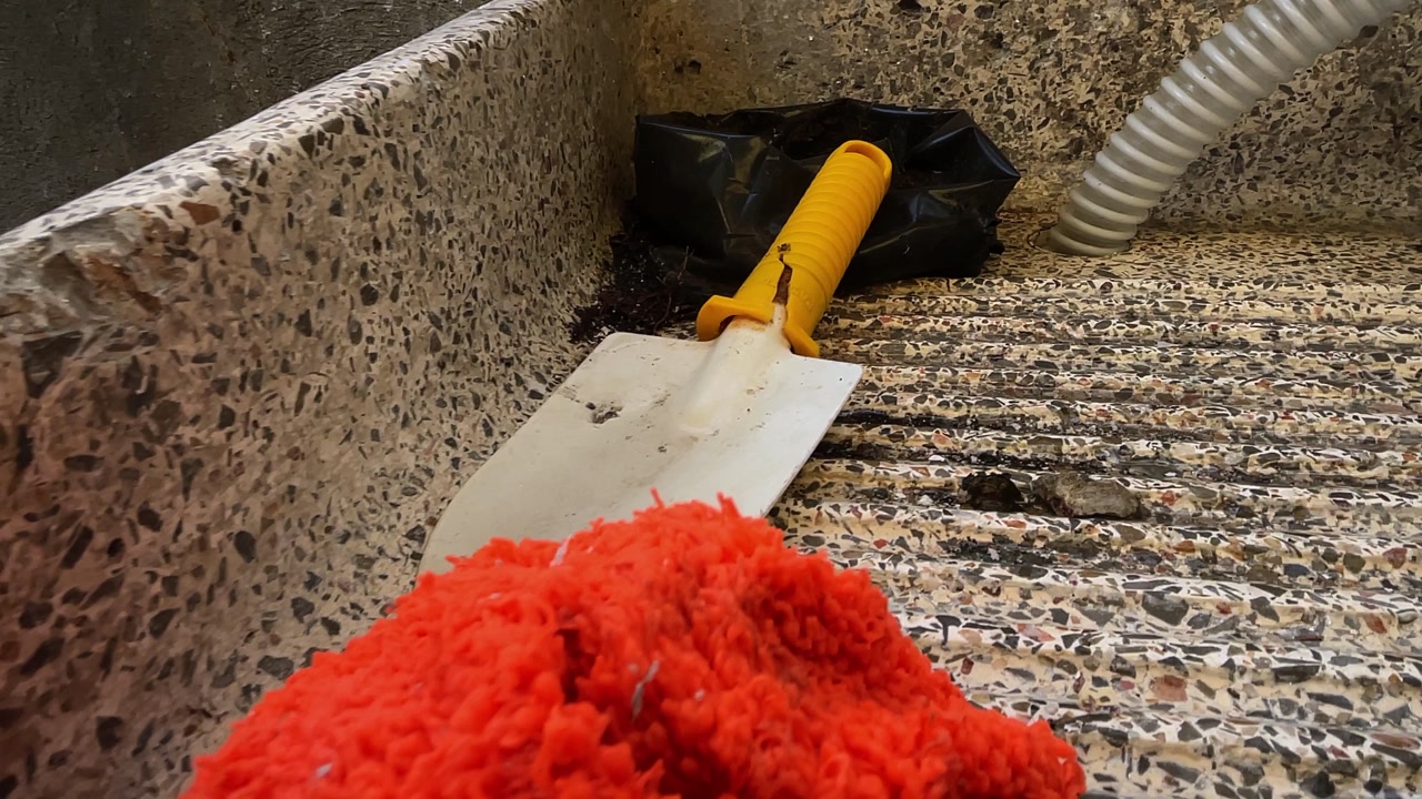 Slow-motion panning shot of broken white and yellow gardening shovel with orange sponge in granite container outside