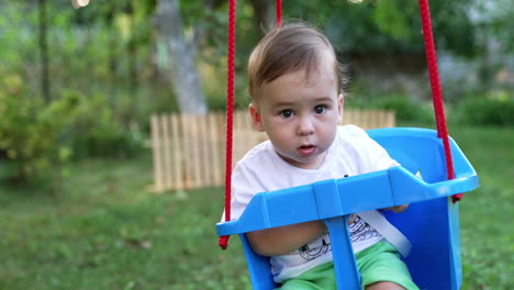 adorable child sitting in a swing. cute kid looks into camera and then at fastener from a swing. close up.