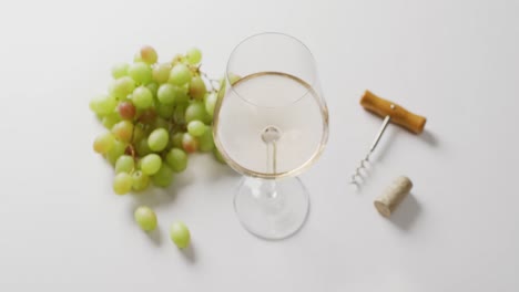 vaso de vino blanco, sacacorchos y uvas sobre una superficie blanca con espacio para copiar