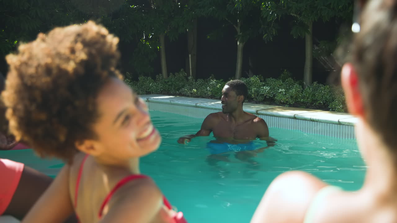 Diverse friends enjoying sunny day by pool, laughing and relaxing with drinks