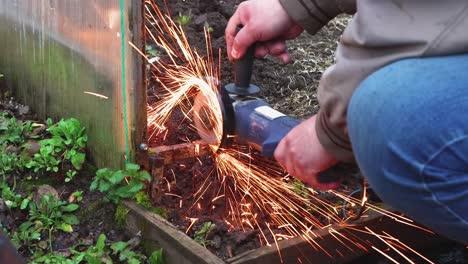 primer plano de un hombre con una molienda angular cortando un viejo invernadero de metal.