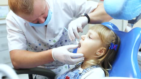 Children's dentist doctor in white gloves examines the teeth of a little blonde girl. Visit to the dental clinic
