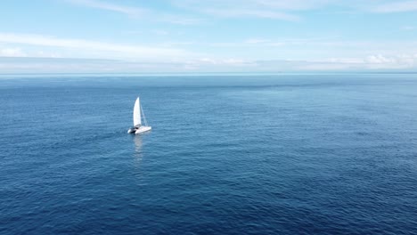 flying towards a small yacht as it slowly sails through a flat ocean