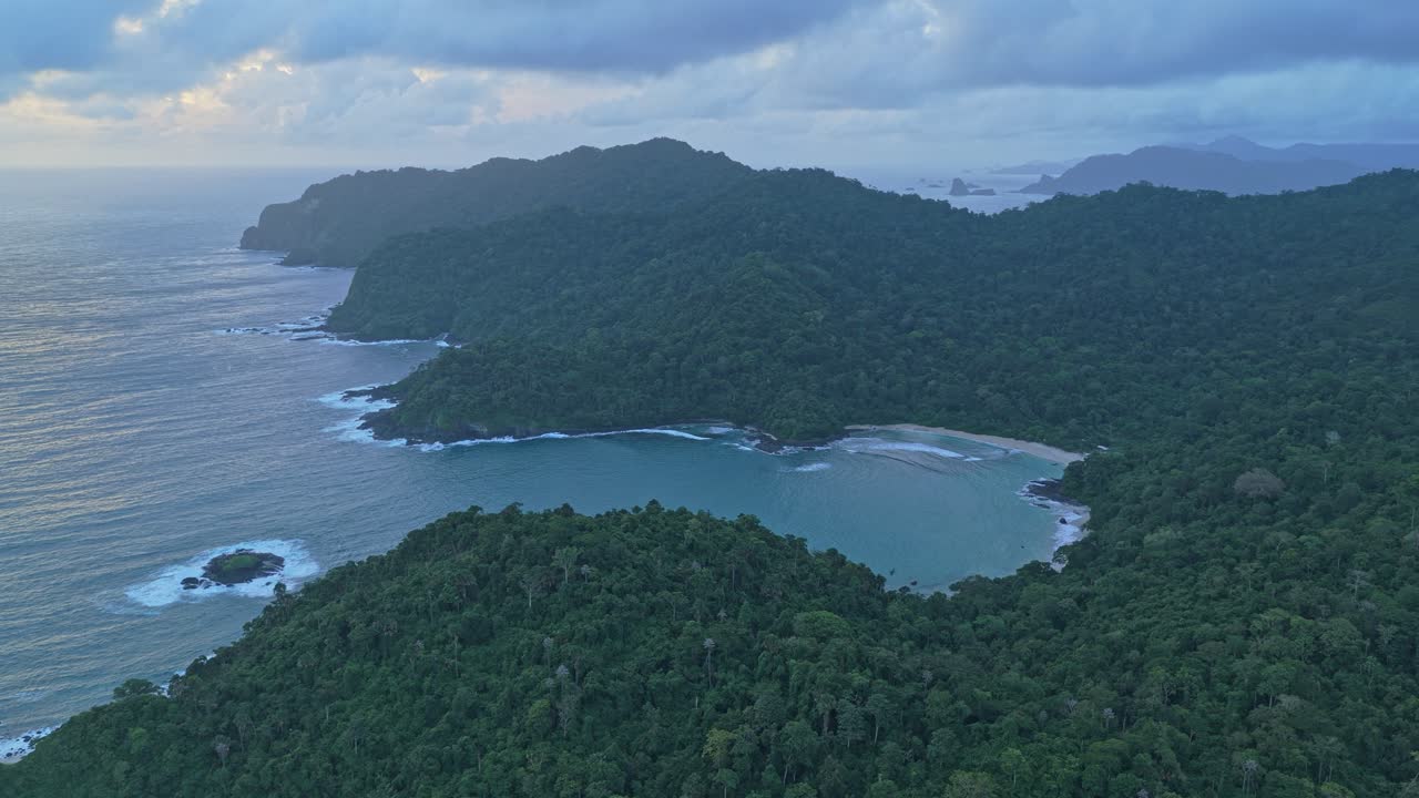 Spettacolare prospettiva aerea della costa frastagliata dell'isola rossa a Giava, che mostra una baia isolata con acqua turchese e una fitta giungla verde.
