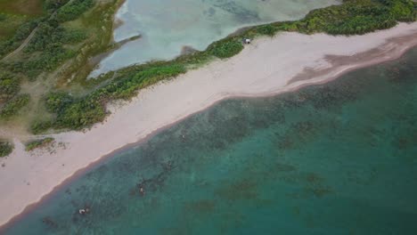 drone footage of flying over a beach, captures a car parked, a camping tent set up, a vast expanse of the beach, beautiful scenery and clear blue water