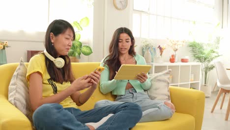 two women using technology while relaxing on a sofa