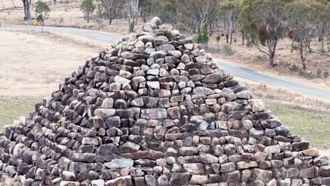 drone camera steadily approaches a large granite rock pyramid in a dry, open landscape with scattered trees and overcast daylight