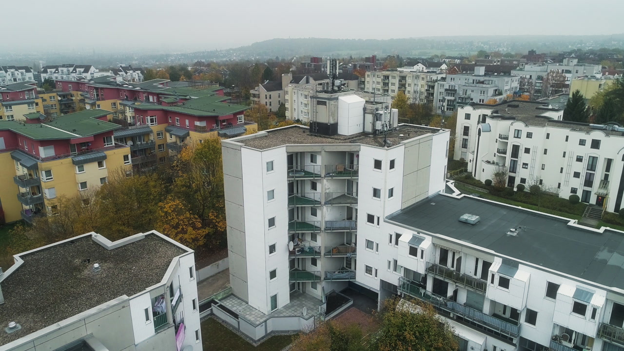 Drone panning over a residential neighborhood with apartment buildings and autumn trees under a cloudy sky in Germany