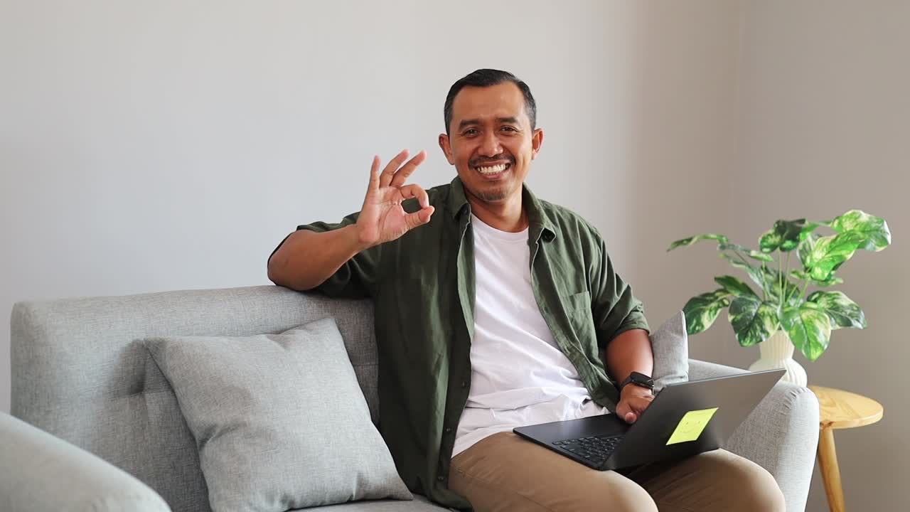 Asian freelancer showcasing positive emotion and displaying ok gesture with fingers in home workspace