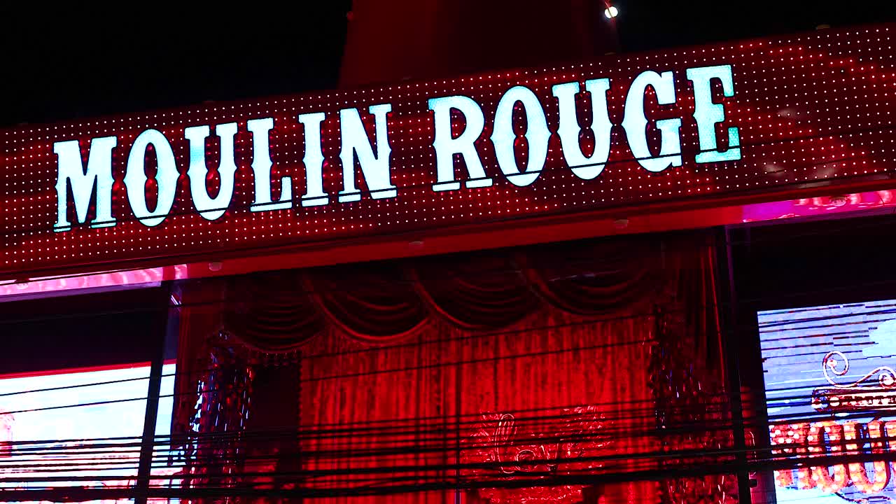 Brightly lit Moulin Rouge sign and windmill in Phuket's vibrant nightlife scene, captured with dynamic camera angles and vivid colors