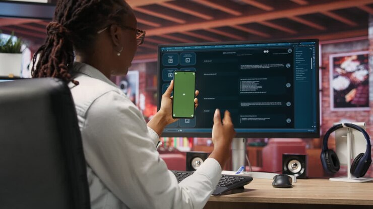 Woman seated at desk using AI LLM chatbot software and green screen phone