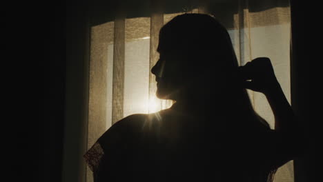 Silhouette-of-a-middle-aged-woman-combing-her-hair-at-the-window