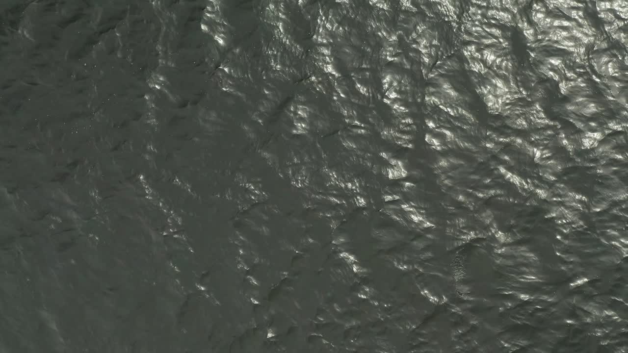 Aerial top down, very dark green gray ocean lake water, small waves rippling