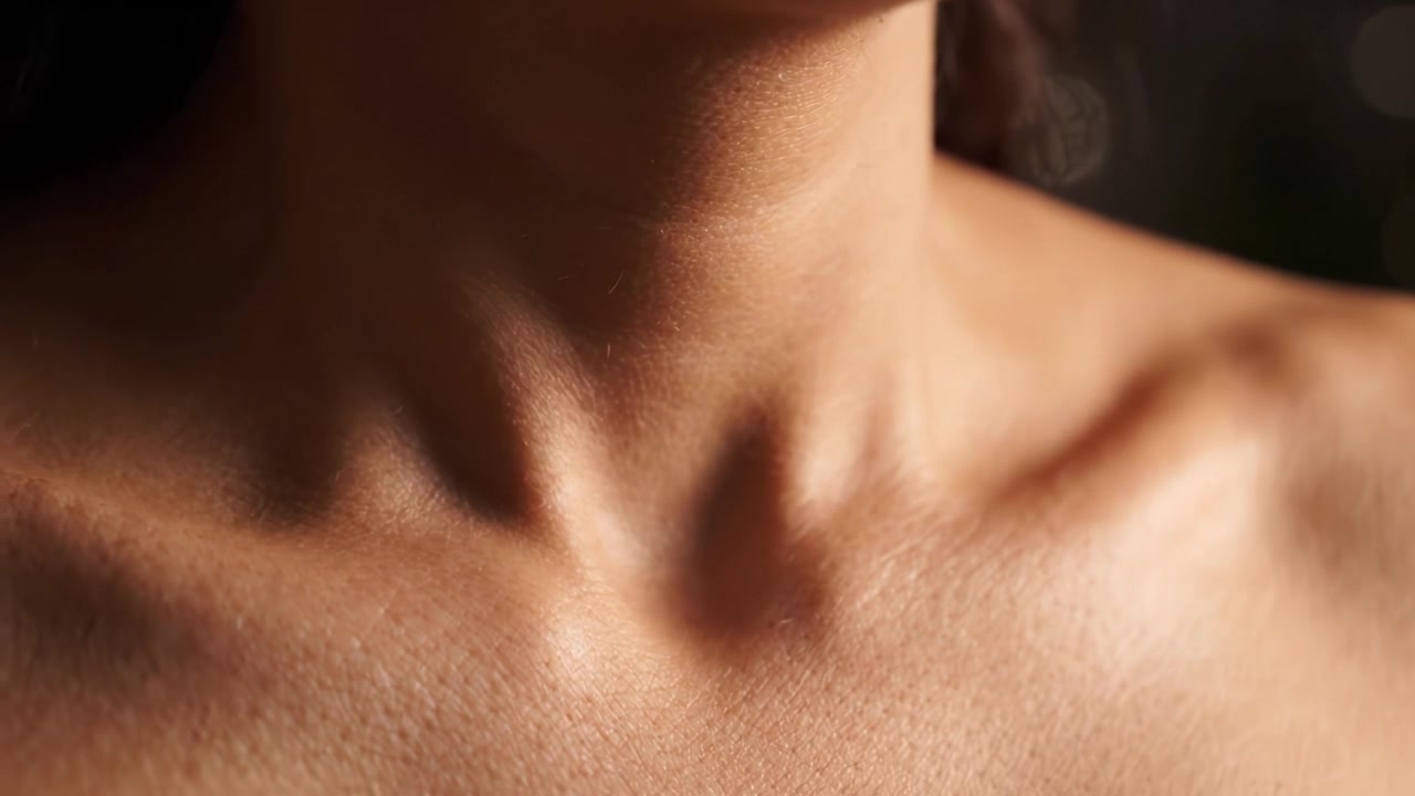 Una vista ravvicinata che evidenzia i contorni e la texture del collo umano, concentrandosi sulla bellezza naturale e sui dettagli sottili della pelle in una luce soffusa.