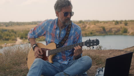 Man playing guitar outdoors by a lake