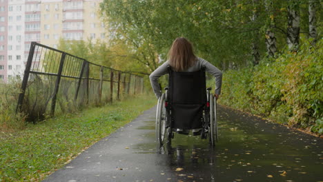 mujer en silla de ruedas camina por el camino en el parque en un día lluvioso