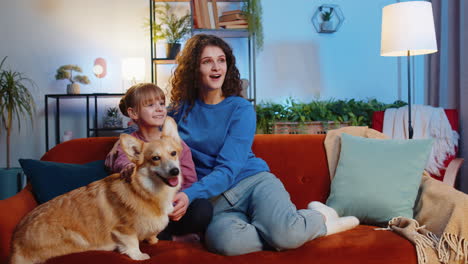 happy family mother and daughter sitting beside corgi dog watching tv in living room at home