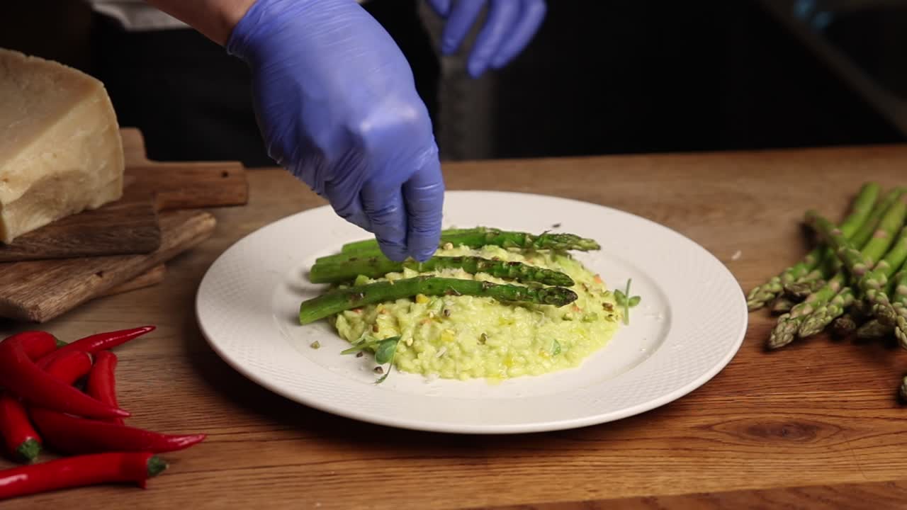 Chef che guarnisce risotto agli asparagi con formaggio grattugiato