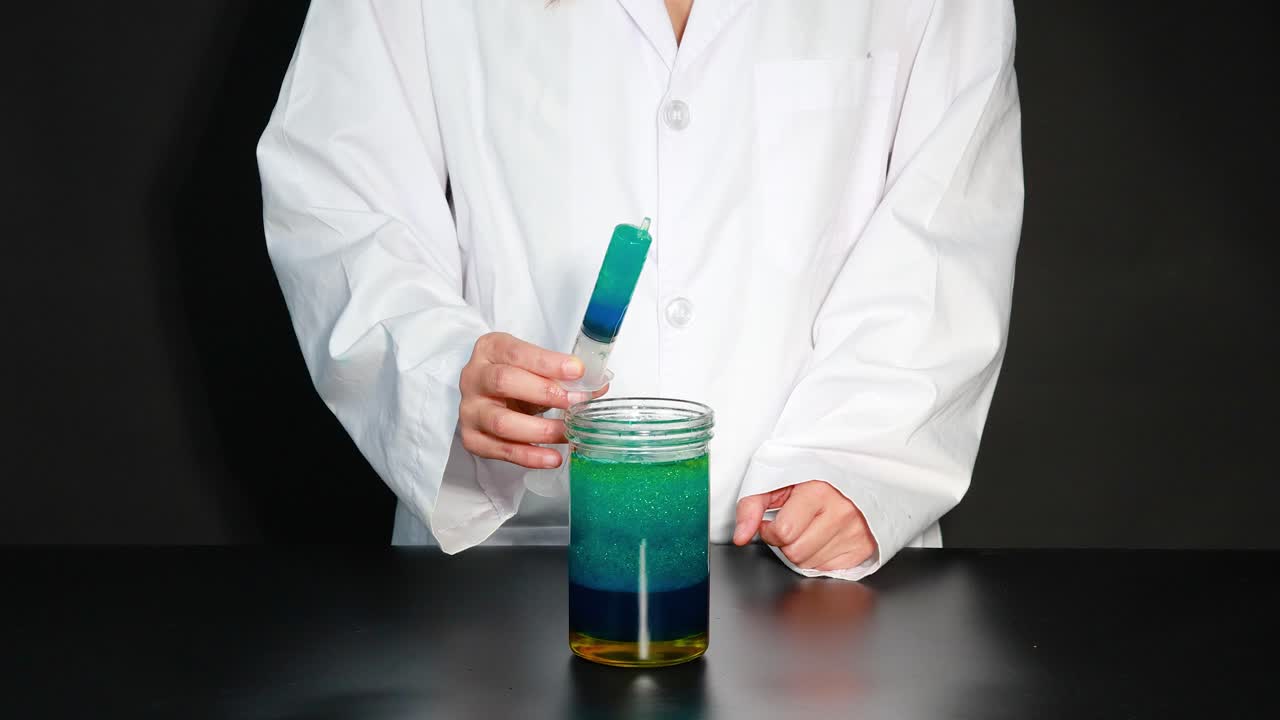 A scientist uses a syringe to create a lava lamp effect in a jar, demonstrating fluid dynamics
