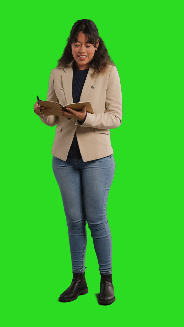 Žena stojí před zeleným plátnem a drží zápisník a propisku.