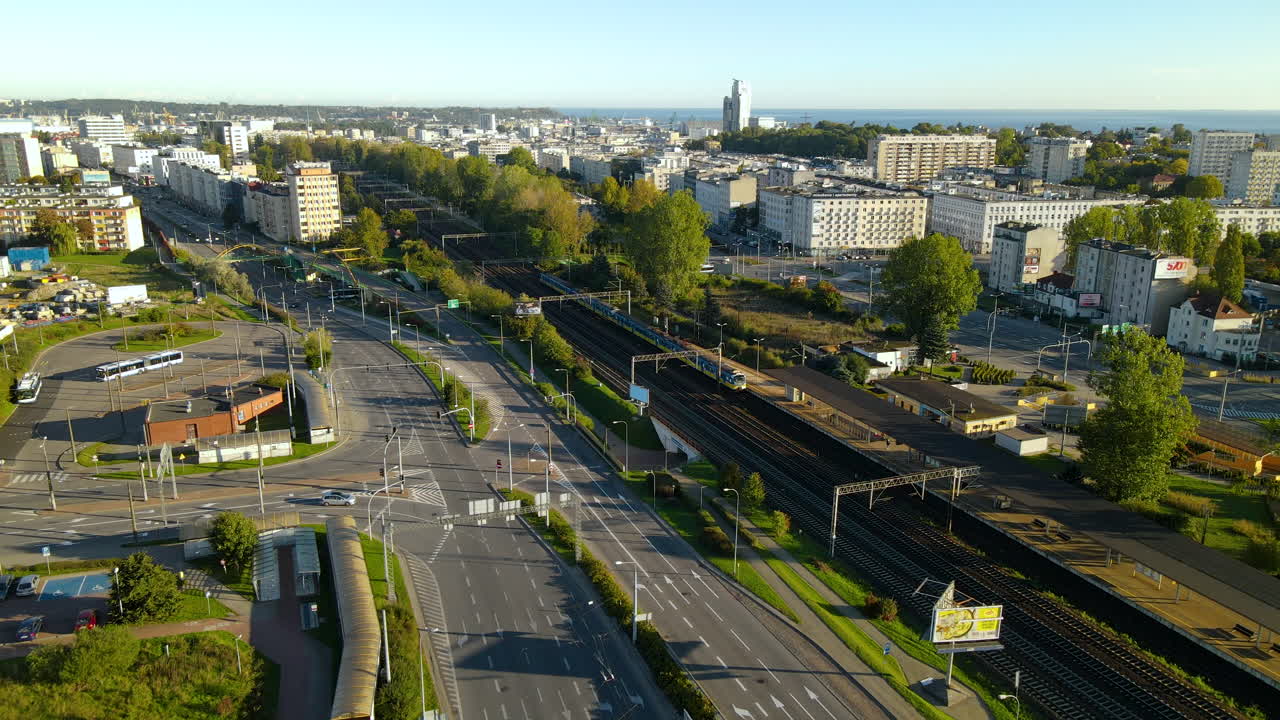 Aerial flyover Gdynia City during sunny day with driving cars on main road and train on rails,Poland