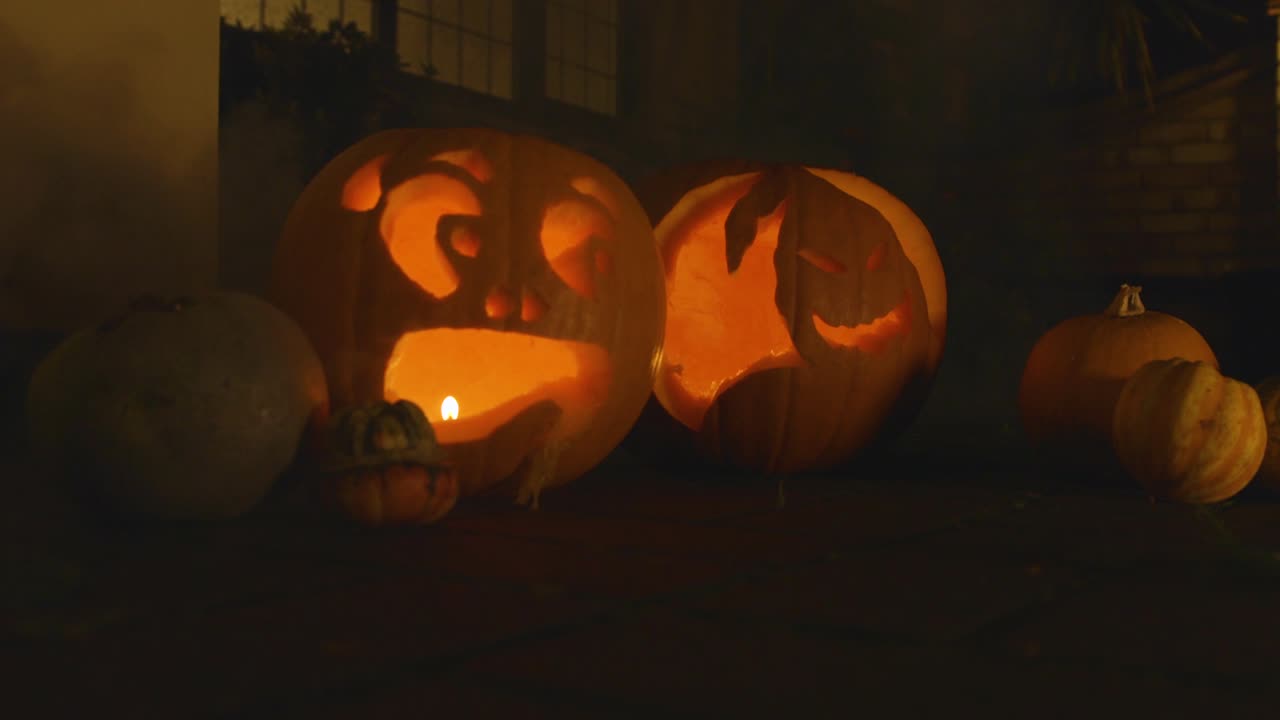 2 carved lit pumpkin outside the front of a house Halloween with smoke with little pumpkins slow motion