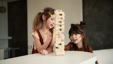 Two-preteen-girls-friends-children-playing-board-game-Jenga-on-table-in-kitchen-at-home