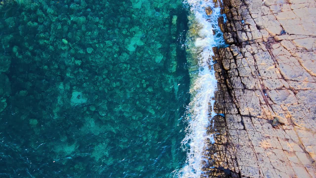 A breathtaking aerial shot capturing the intricate interplay between vibrant azure waters and cracked, earthy rock formations along the Tunisian coastline.