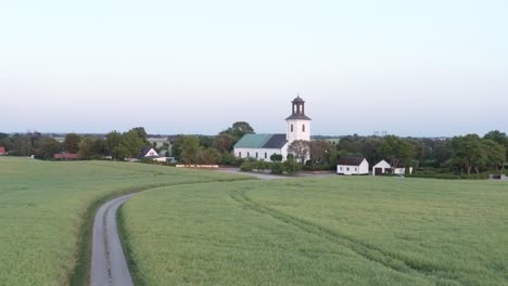 Drone-shot-of-church-with-rapeseed-fields-in-the-foreground-in-Skane,-Southern-Sweden