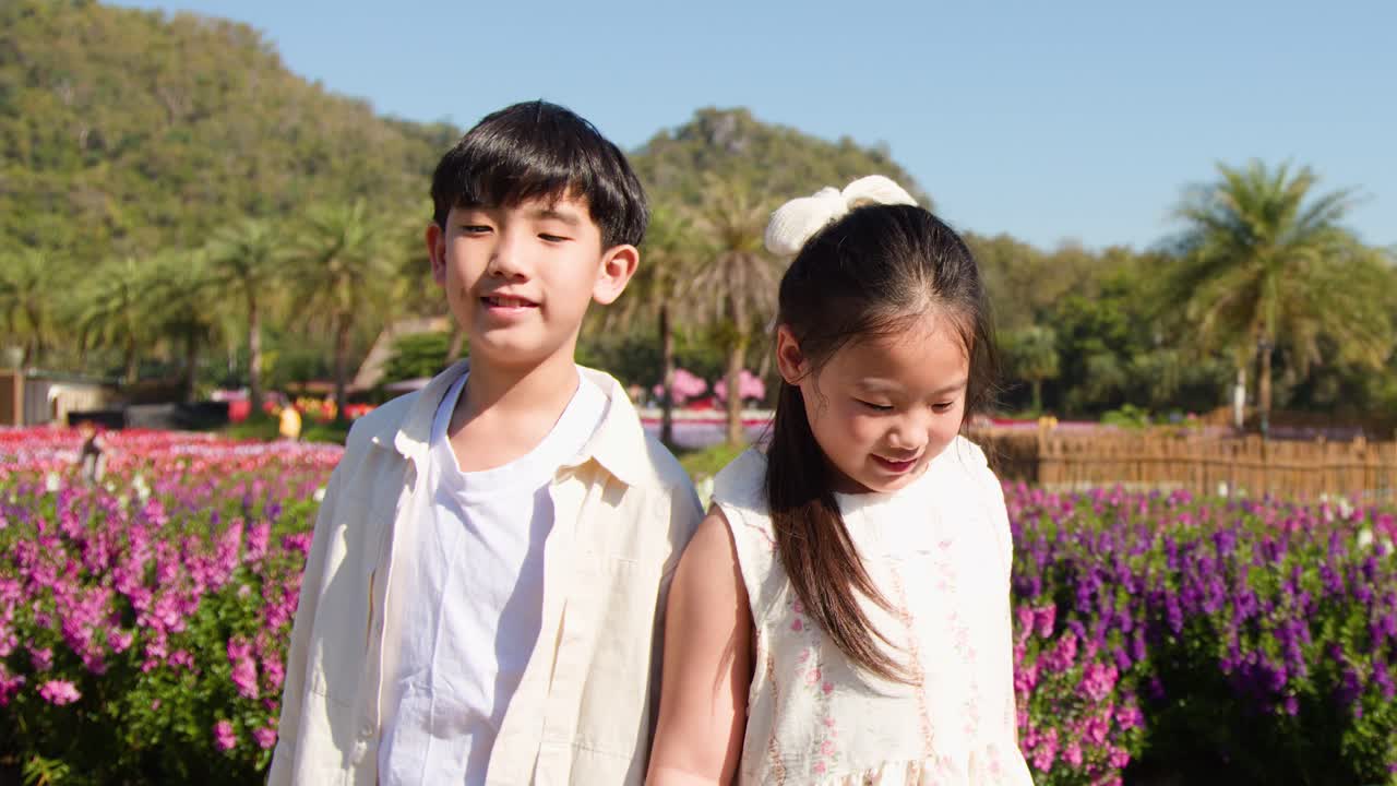 タイで、明るい日差しの下、鮮やかな花畑の中を2人の幼い子どもたちが歩いています
