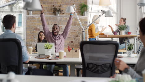 Hombre-De-Negocios-Con-Los-Brazos-Levantados-Celebrando-El-éxito-Viendo-La-Victoria-Deportiva-En-Una-Computadora-Portátil-Grupo-Diverso-De-Personas-Aplaudiendo-Expresando-Entusiasmo-En-La-Oficina