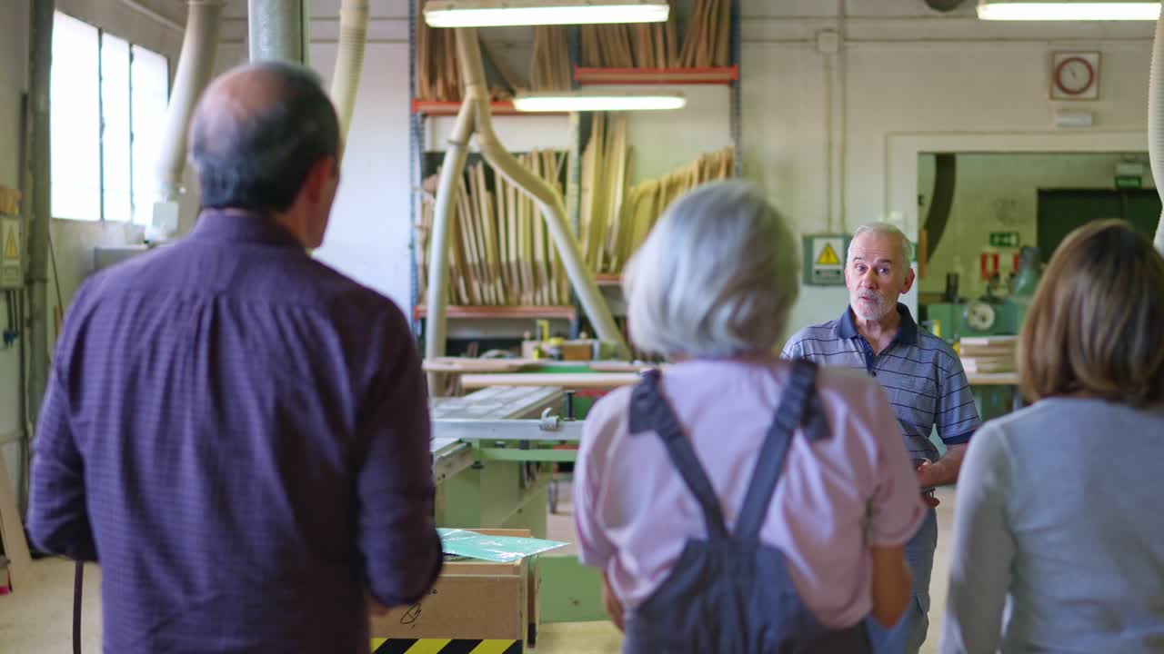 Senior Man Discussing with Group of Workers in Woodworking Workshop