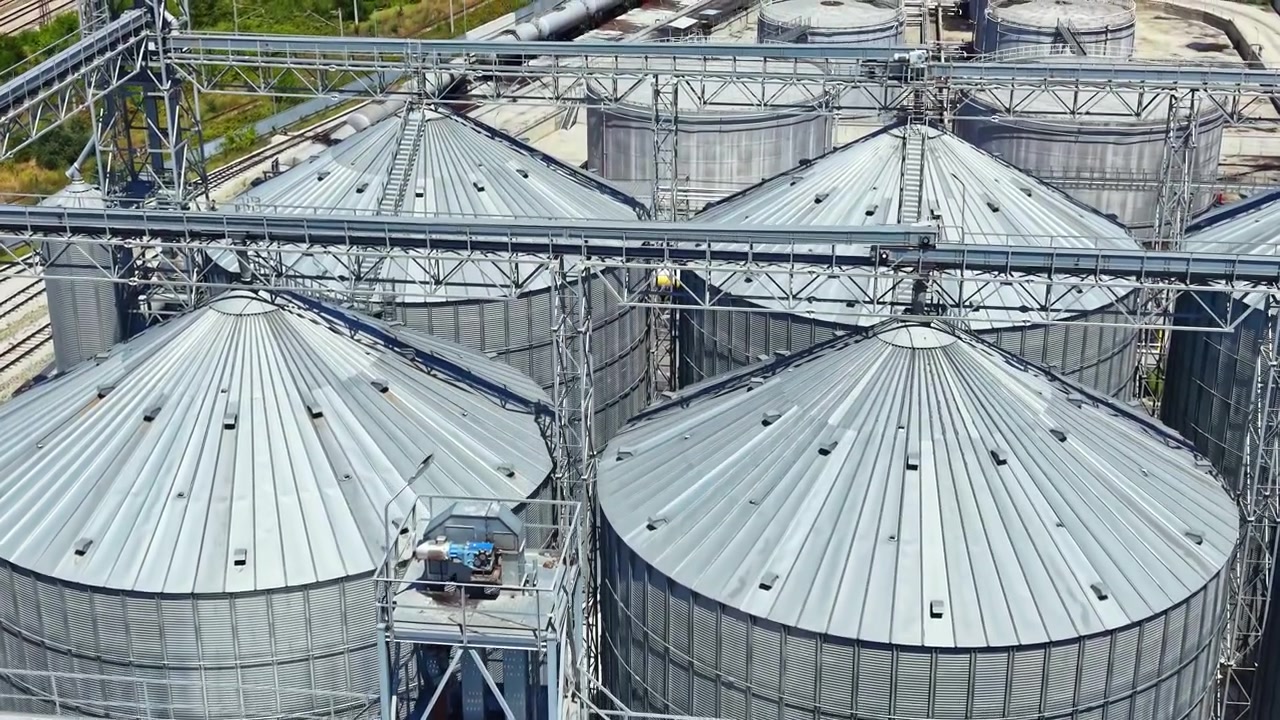 Silos stand tall at a grain storage facility in bright sunlight, showing their metal roofs and strong structures against a clear sky