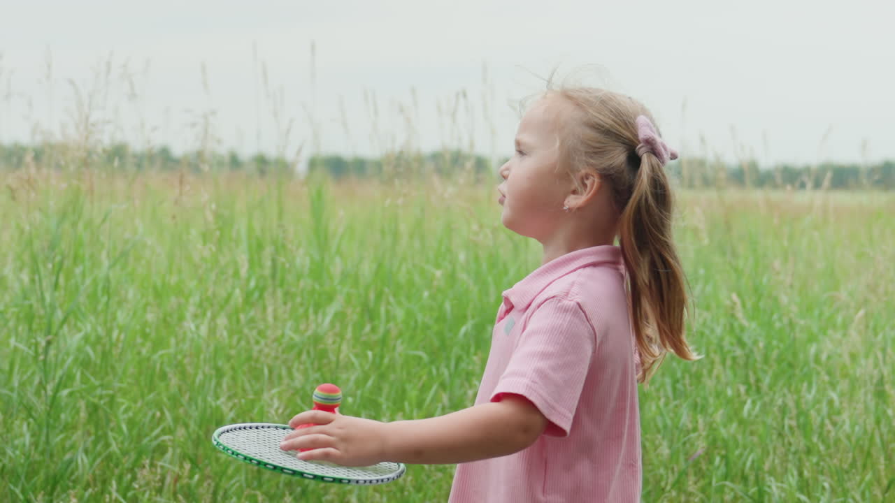 Una chica blanca explorando la hierba en una pradera, inclinándose para examinar plantas y bádminton, ambiente tranquilo y apacible con tallos verdes altos, polo rosa y pantalones cortos de mezclilla, maravillosa reflexión veraniega en el campo