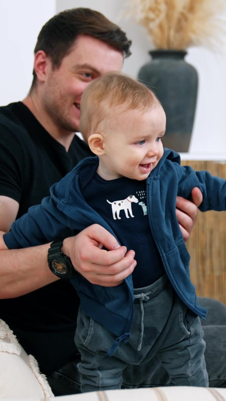 Uomo caucasico sorridente con un bambino in braccio. Il piccolo neonato impara a stare in piedi sostenuto dal padre. Video verticale