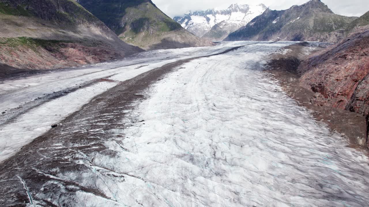 Voo panorâmico aéreo épico sobre uma vasta geleira alpina Aletsch, morenas escuras fluindo como rios através do gelo antigo, emolduradas por picos imponentes em uma paisagem montanhosa dramática da Suíça por drone 4k.