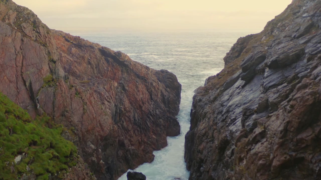 Aerial dolly shot moves forward, showcasing intricate rock formations, tilting up to reveal the Atlantic Ocean at Malin Head