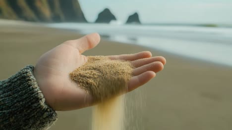 close-up of a hand letting sand fall on a beach, captured from a side angle