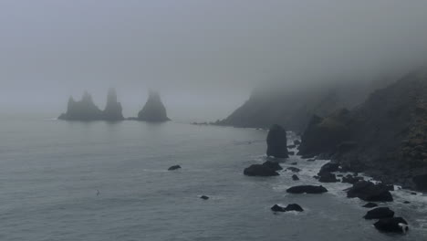 Luftaufnahmen,-Filmischer-Langsamer-Schwenk,-Linke-Wellen,-Krachende-Heuhaufen-Bei-Vik,-Island,-Früher-Winternebel-Am-Schwarzen-Sandstrand,-Wellen,-Die-An-Der-Küste-Krachen