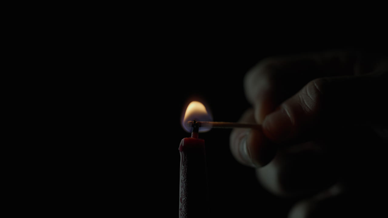 Hand holding wooden match to light paraffin candle on black background closeup