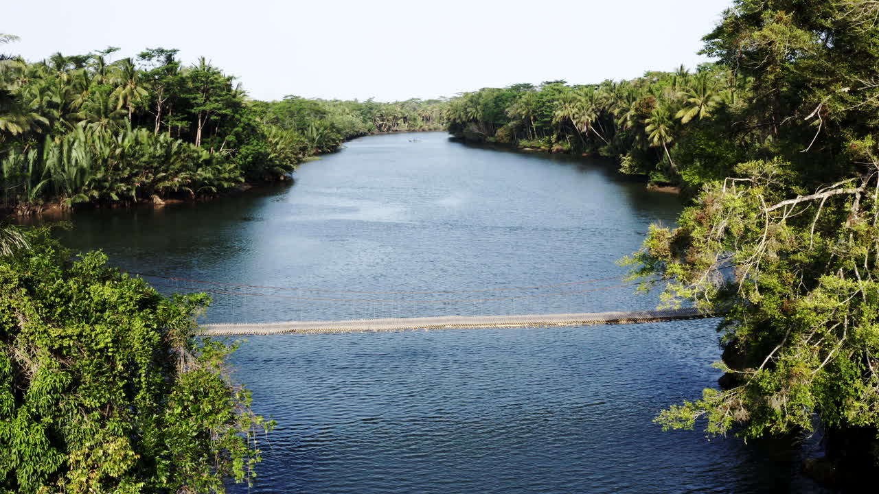 Motorcyclist crossing a suspension bridge over a river in a tropical forest