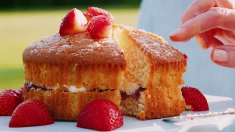 close up of woman cutting slice of strawberry sponge cake