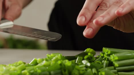 cutting fresh green onions on a cutting board, close up chef cooking green vegan salad.
