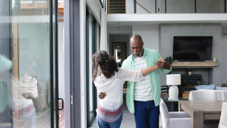 happy biracial couple holding hands and dancing in living room, slow motion