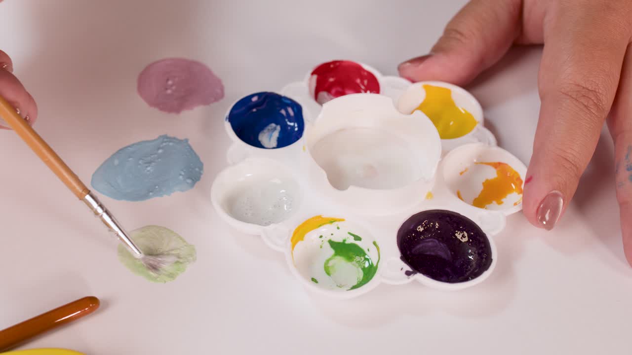 Hand mixes watercolor paints on palette, creating new color, under bright, even studio lighting